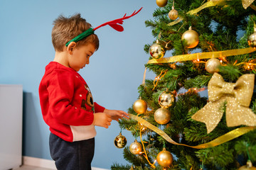 Side view of small boy two or three years old decorating christmas tree at home new year holiday concept