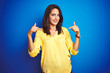 © Krakenimages.com - Young beautiful woman wearing yellow t-shirt standing over blue isolated background looking confident with smile on face, pointing oneself with fingers proud and happy.