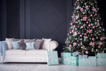 Contemporary Christmas (New Year) interior design: fir tree decorated with pink and turquoise balls, gift boxes laying on wooden floor under it, white sofa with pillows against wall. Winter holidays