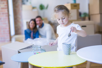 Beautiful family sitting on the floor playing with his kid at new home around cardboard boxes