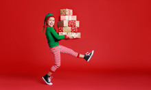 Cheerful Funny Child In Christmas Elf Costume With Gifts On   Red Background.