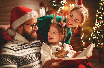 Wall Mural - Christmas Eve. family father, mother and child reading magic book at home .