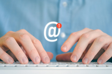 A man in a shirt in front of the keyboard. Abstract email icon with new message.