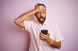 Young indian man using smartphone standing over isolated pink background stressed with hand on head, shocked with shame and surprise face, angry and frustrated. Fear and upset for mistake.