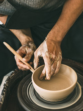 Ceramist At A Pottery Workshop Man Is Sculpting A Bowl Behind A Rotating Potter's Wheel