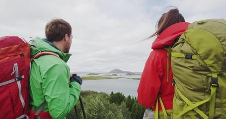 Wall Mural - Travel and hiking couple looking at view. People on hike by lake outdoors wearing backpacks trekking in beautiful nature landscape. Active young couple living healthy lifestyle by Lake Myvatn, Iceland