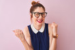 Redhead woman with pigtail wearing elegant dress and glasses over isolated pink background very happy and excited doing winner gesture with arms raised, smiling and screaming for success. 