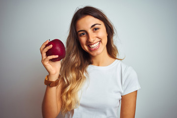 Wall Mural - Young beautiful woman eating red apple over grey isolated background with a happy face standing and smiling with a confident smile showing teeth