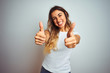 © Krakenimages.com - Young beautiful woman wearing casual white t-shirt over isolated background success sign doing positive gesture with hand, thumbs up smiling and happy. Cheerful expression and winner gesture.
