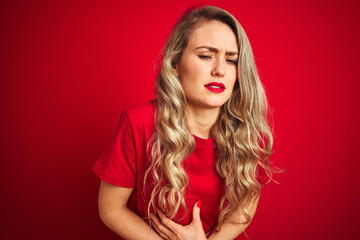 Poster - Young beautiful woman wearing basic t-shirt standing over red isolated background with hand on stomach because indigestion, painful illness feeling unwell. Ache concept.