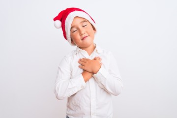 Sticker - Beautiful kid boy wearing Christmas Santa hat standing over isolated white background smiling with hands on chest with closed eyes and grateful gesture on face. Health concept.