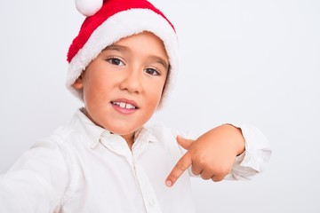 Sticker - Beautiful kid boy wearing Christmas Santa hat make selfie over isolated white background with surprise face pointing finger to himself