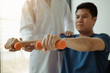 © wutzkoh - Asian physiotherapist helping a patient lifting dumbbells work through his recovery with weights in clinic room.