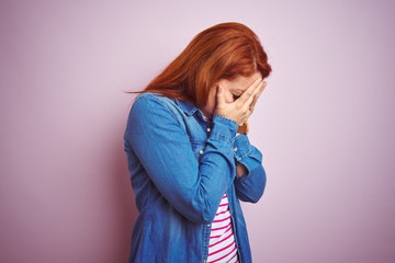 Wall Mural - Beautiful redhead woman wearing denim shirt and striped t-shirt over isolated pink background with sad expression covering face with hands while crying. Depression concept.