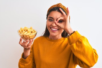 Wall Mural - Young beautiful woman holding bowl with macaroni pasta over isolated white background with happy face smiling doing ok sign with hand on eye looking through fingers