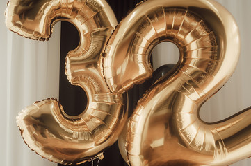 decor for the holiday. gold foil balloons, numbers 32 against the background of black curtains, white tulle 