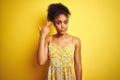African american woman wearing casual floral dress standing over isolated yellow background Shooting and killing oneself pointing hand and fingers to head like gun, suicide gesture.