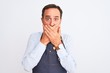 © Krakenimages.com - Middle age shopkeeper man wearing apron standing over isolated white background shocked covering mouth with hands for mistake. Secret concept.