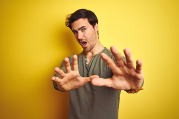 Wall Mural - Young handsome man wearing casual t-shirt standing over isolated yellow background afraid and terrified with fear expression stop gesture with hands, shouting in shock. Panic concept.