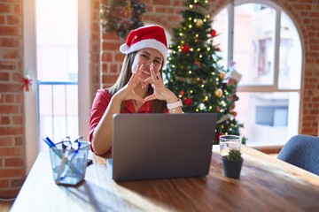 Canvas Print - Beautiful woman sitting at the table working with laptop wearing santa claus hat at christmas smiling in love showing heart symbol and shape with hands. Romantic concept.