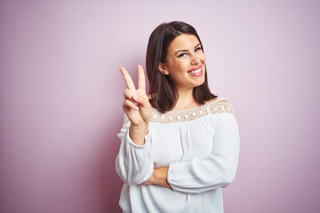 Sticker - Young beautiful brunette woman over pink isolated background smiling with happy face winking at the camera doing victory sign. Number two.