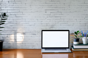 Mockup laptop with blank screen, houseplant and stack of book on wooden table, blank screen for graphic design.