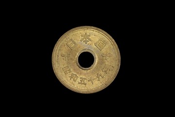 A close up, macro image of golden, Japanese five yen coin isolated on a black background