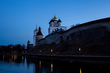 Night panorama of the city. Lanterns illuminate the walls and towers of the medieval fortress with a bell tower and a Cathedral which are reflected in the water of the river. Pskov, Russia.