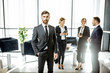 © rh2010 - Portrait of a handsome white collar worker standing in front of business team at the luxurious office