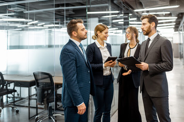 Wall Mural - Group of business people strictly dressed in the suits meeting in the hallway of the modern office building, white-collar workers having informal discussion indoors