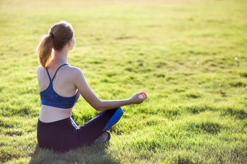 Wall Mural - Young sportive woman in yoga position meditates in field at sunrise.