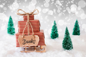 Wall Mural - Sled With Christmas Gift And Label With German Danke Means Thank You. Snow With Christmas Tree And Gray Sparkling Background