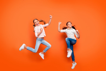 Canvas Print - Full length photo of positive rejoicing two girlfriends jump rest relax win school sport competition raise fists wear white shirt denim jeans isolated over orange color background