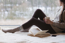 Thoughtful Young Brunette Woman With Morning Cup Of Coffee Looking Through The Window, Blurry Winter Outside. 