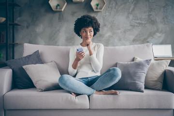 Wall Mural - Photo of pretty dark skin wavy lady homey atmosphere holding telephone author thinking dreamy inspiration moment sitting cozy couch casual outfit flat loft indoors