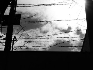 black and white picture, light and sky are visible behind barbed wire