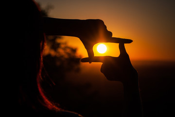 hands folded in a frame on a sunset background