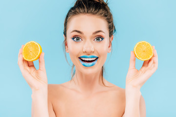 Wall Mural - excited naked beautiful woman with blue lips holding orange halves isolated on blue