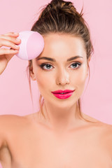 naked beautiful woman with pink lips holding facial cleansing brush isolated on pink