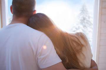 Young couple in love woman man embracing holding home by the window. Snowing winter christmas concept