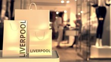 Paper Shopping Bags With Liverpool Caption Against Blurred Store Entrance. Retail In The United Kingdom Related Conceptual 3D Animation
