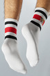 Close-up back shot of male ankles in white crew ribby socks with red and black stripes and an embroidered tiger head. The feet are isolated on the gray background.