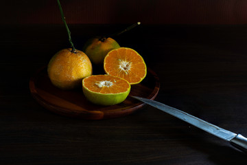 Oranges in the brown wooden tray on dark background which has dim light