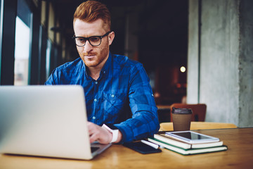 Caucasian male remote worker installing application for organize weekly schedule connected to free cafeteria wifi during leisure time,serious man in spectacles reading received message from colleague