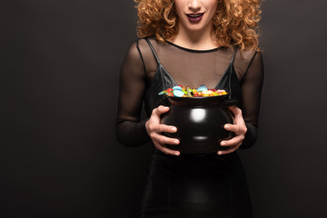 cropped view of woman holding pot with candies for halloween on black