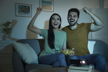 Canvas Print - Emotional young couple watching TV using video projector at home