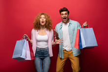 Excited Beautiful Couple Holding Shopping Bags, Isolated On Red