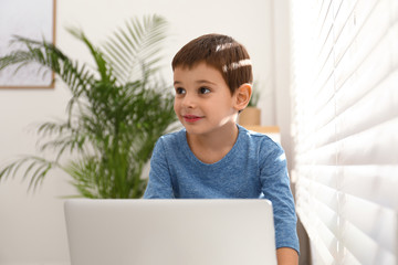 Poster - Happy little boy with modern laptop near window indoors