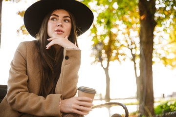 Poster - Portrait of attractive woman sitting on bench with coffee cup in autumn park