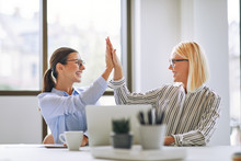 Two Smiling Businesswomen High Fiving Together In An Office